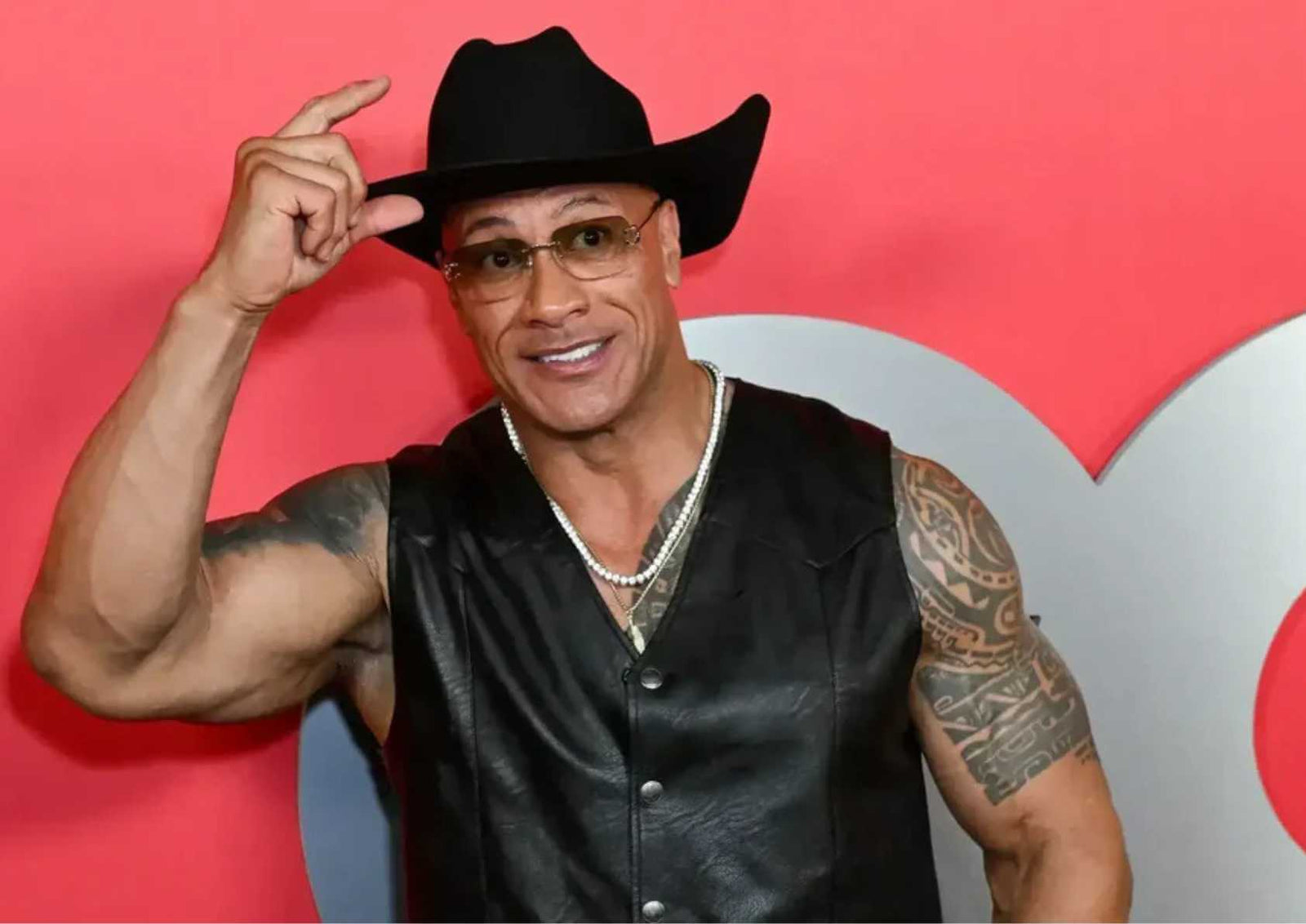 Dwayne Johnson wearing a cowboy hat and leather vest, smiling at a red carpet event.